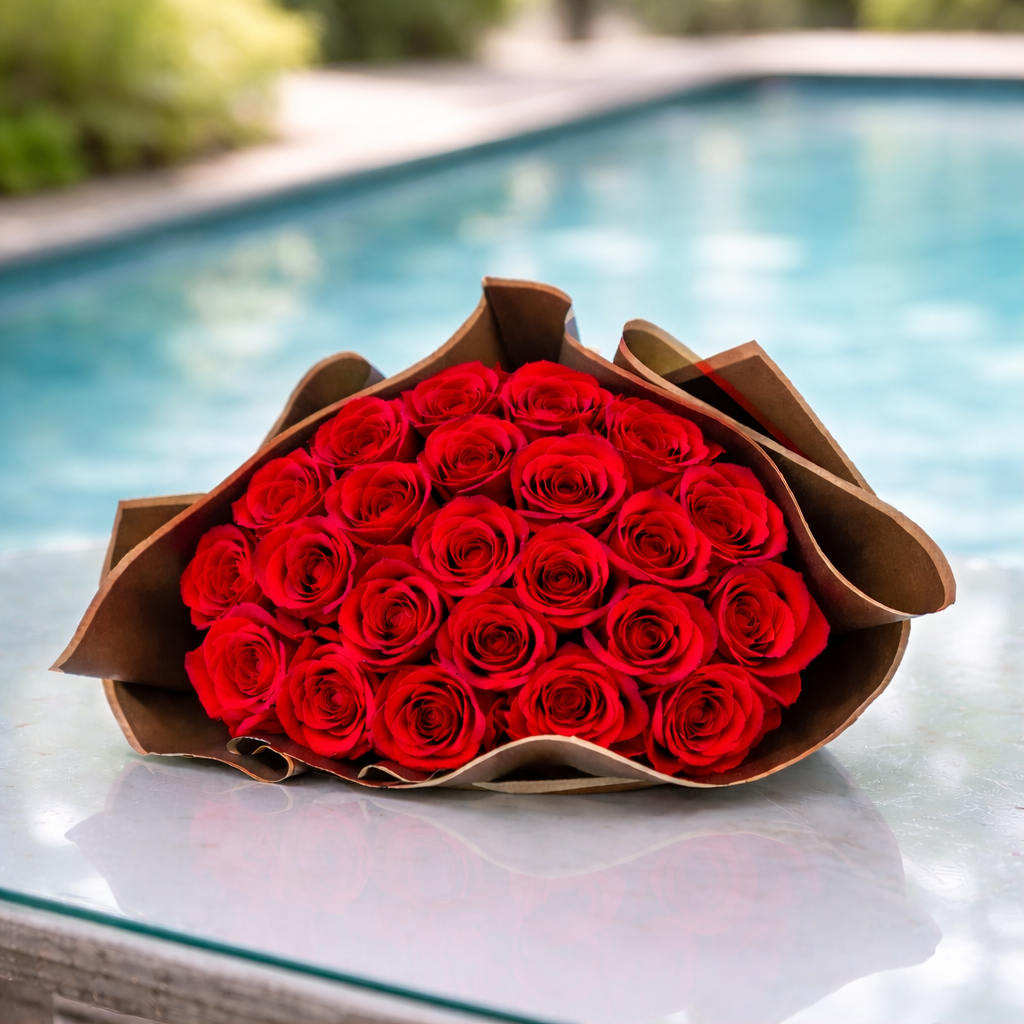 Ramo de 24 rosas rojas sobre mesa de cristal junto a piscina en ambiente exterior elegante
